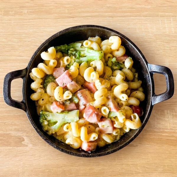 Macaroni and cheese with ham and broccoli florets in a black cast iron skillet on a wooden table.