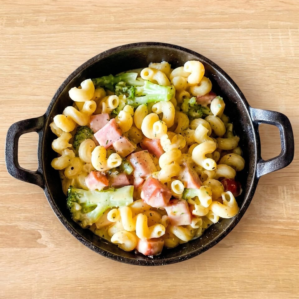 Macaroni and cheese with ham and broccoli florets in a black cast iron skillet on a wooden table.